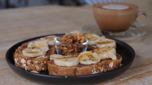 バナナと蜂蜜の全粒トーストで構成される栄養価の高い朝食のクローズアップはアーモンドスライスでトッピングされ 現代の黒板で提供されました 健康的な食べ物とライフスタイル — ストック動画