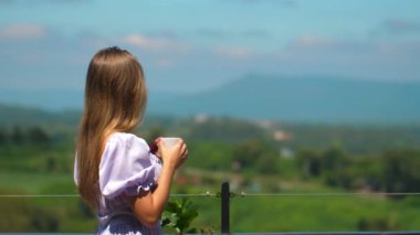 Elinde kahve fincanı tutarken yemyeşil manzaraya tepeden bakan, balkonda duran huzurlu kadın. Rahatlama ve sükunet.