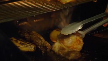 Koyu barbekü ortamında açık ateşte ızgara tavuk. resim, terbiye edilmiş kümes hayvanlarının maşa, vurgu tekniği ve açık havada pişirmede kullanılan araçlarla çevrildiğini gösteriyor.