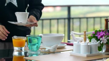 Garson, çay, meyve suyu ve zarif sofra takımlarını içeren manzaralı terasta bol bol kahvaltı servisi yapıyor. Açık hava yemek deneyimi. Sabah atmosferini yemek ve manzara güzelliği ile yakalamak..