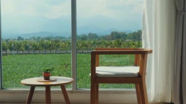 Minimalist yaşam alanı ahşap mobilyaları, geniş pencereli yemyeşil alanlar ve arka planda dağlar, doğa ile barış ve bağlantı duygusunu çağrıştırıyor. İç Tasarım ve Huzur.