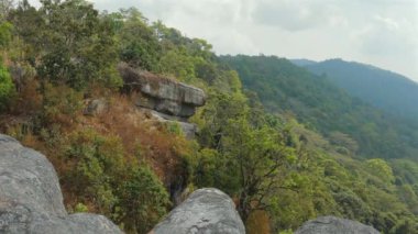 Arkaplanda bulutlu gökyüzü olan yemyeşil orman ve kaya oluşumlarının manzarası doğal güzellikleri ve açık hava keşiflerini gözler önüne seriyor. Doğa ve Macera.
