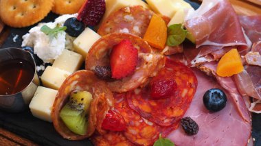 Çeşit çeşit peynirler, soğuk kesimler, taze meyveler ve krakerler içeren lezzetli şarküteri panosunun yakın plan görüntüsü. Gourmet aperatifleri ve aperatifler için güzelce hazırlanmış. Yemek ve Mutfak Sanatı.
