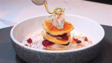 Çırpılmış kremayla kaplı gurme kreplerinin üzerine akçaağaç pekmezi dökmek, modern mutfak tezgahının üzerine seramik kasede taze böğürtlen koymak. Yemek ve Mutfak Sanatı.