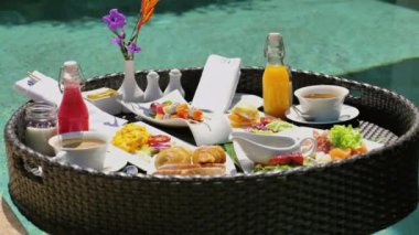Tropik tatil beldesindeki yüzme havuzunda lüks yüzen kahvaltı tepsisi. Taze meyve, hamur işi, meyve suyu ve sıcak içeceklerle gurme bayramı deneyimi. Egzotik bir tatil yemeği ve eğlence..