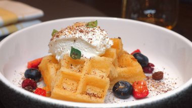 Krem şanti, taze yaban mersini, çilek ve beyaz kasede çikolata parçacıkları ile kaplı lezzetli altın waffle 'lar kahvaltı ya da brunch fikirleri için mükemmel. Sağlıklı Yeme ve Yaşam Tarzı.