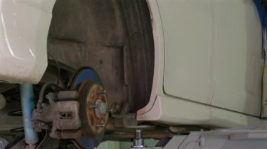 Garajda tamirat yapılan arabanın kapatılması, parçalanmış tekerlek ve fren sistemine odaklanılması, bakım ve makine mühendisliğinin vurgulanması.