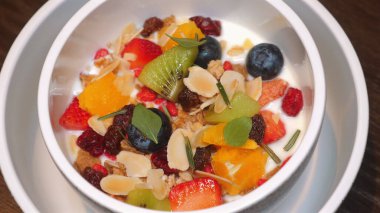 Renkli ve sağlıklı meyve kasesini yoğurtlu, taze böğürtlenli, kivili, bademli ve kuru meyveli, beyaz kasede servis edilen, ahşap masada içilen. Sağlıklı Yeme ve Yaşam Tarzı.