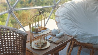 Hasır sandalyeli ve minderli oturma odalı rahat bir açık hava koltuğu, sakin doğa ortamında hamur işleri ve sandviçlerle birlikte zarif bir ikindi çayı seti, rahatlama ve rahatlama..