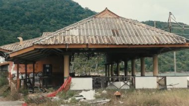 Kırık çatılı terk edilmiş bir pavyon, otlar ve dağların önüne serilmiş molozlar..