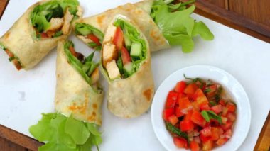 Marul, domates ve beyaz tabakta salatalıklı taze tavuk paketleri yanında da doğranmış domates ve otlar..