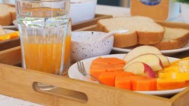 Taze meyveli kahvaltı tepsisi, bir dilim ekmek, bir bardak portakal suyu ve yoğurt, ahşap tepside sıralanmış, sağlıklı ve besleyici yemek ortamı yaratıyor. Sağlıklı Yeme ve Yaşam Tarzı.