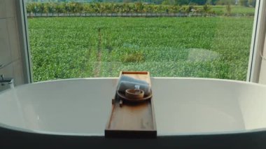 Geniş pencereli yemyeşil alanlar manzaralı lüks bir küvet. Huzurlu ve rahatlatıcı bir atmosfer yaratıyor. Spa ve Sağlık..