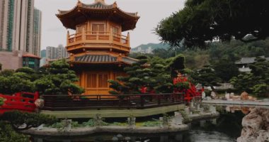 Çadırı, kırmızı köprüsü, yemyeşil bahçesi ve göleti olan geleneksel Çin bahçesi. Şehir binaları ve arka planda dağ. Huzurlu, sakin, açık hava.