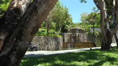 Taştan çağlayan şelale ve yemyeşil mobiletlerin gölgede park edildiği sakin şehir vahası. Modern şehir manzarasında huzur.