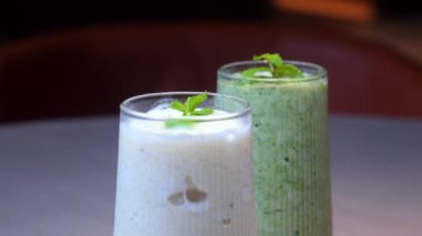 Masada taze nane yapraklarıyla süslenmiş, uzun bardaklarda iki ferahlatıcı meyve püresi. Sağlıklı Yeme ve Yenileme.