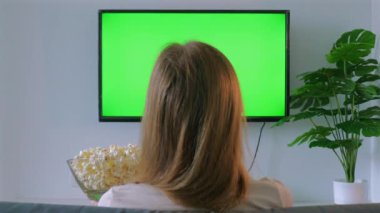 Kanepede oturup, rahat oturma odasında patlamış mısırın, eğlence ve eğlencenin tadını çıkarırken, yeşil ekranlı televizyon izleyen kişinin arkası..