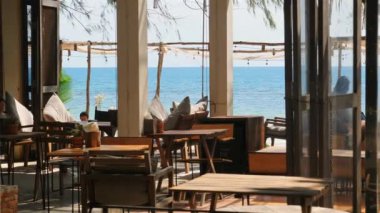 Sahil kenarında ahşap mobilyaları ve manzaralı okyanus manzarası olan rahat bir restoran güneşli bir günde yemek yemek ve dinlenmek için mükemmel bir yer.