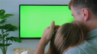 Arka planda yeşil ekranlı bir televizyon izlerken çocuğu kucaklayan bir adam, düzenlenebilir görüntü yaratıyor. Aile Bağları ve Eğlencesi.