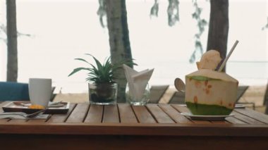 Taze hindistan cevizi, kahve fincanı ve ahşap masa, güneşli gün bitkileriyle tropik plaj kahvaltısı..