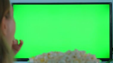 Kadın evde patlamış mısır, sinema ve eğlence yerken yeşil ekran televizyon seyrediyor.