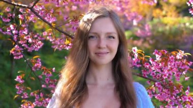 Bahar mevsiminde çiçek açan kiraz ağaçları ya da sakura çiçekleri arasında gülümseyen genç bir kadın. Doğa, güzellik veya seyahat konsepti