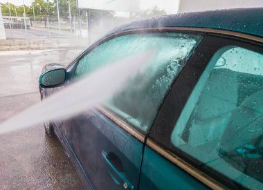 Basınçla yıkanan koyu mavi bir araba. Su jeti yan pencereleri gösteriyor