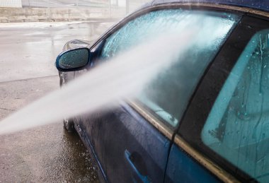 Basınçla yıkanan koyu mavi bir araba. Su jeti yan pencereleri gösteriyor