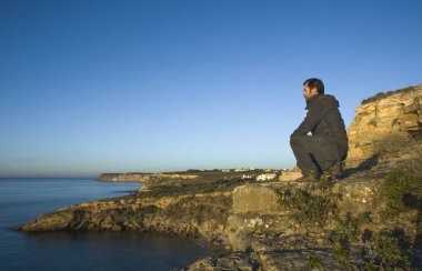 Olgun bir adam uçurumdan güneşin doğuşunu izler. Cama de Vaca uçurumları, Faro Bölgesi, Lagos, Portekiz