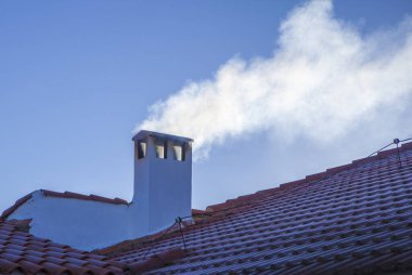 Smoky chimney on a roof covered with winter frost. blue sky background