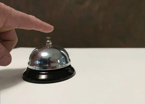 Guest about to press the service bell at the hotel reception. White surface