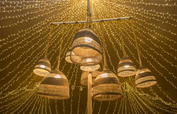 Natural fiber lamps hanging from the ceiling of a tent with a background of LED garlands. Warm atmosphere