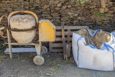 Raffia çimento karıştırıcısının yanına istiflenmiş büyük kum torbası. Kırsal konutlar inşaat endüstrisi konsepti