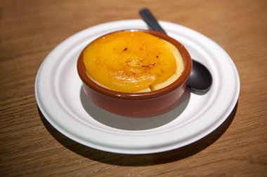 Ahşap arka planda siyah bir kaşıkla kilden bir kasede servis edilen katalan kremi. Seçici odak