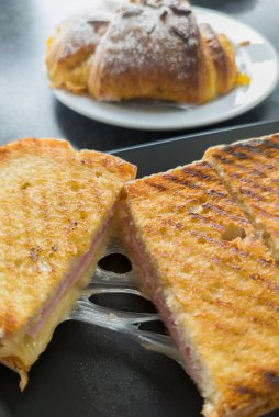 Kızarmış jambonlu ve peynirli sandviç ve altta tatlı çörek. Kahvaltı için tuzlu ve tatlı kombinasyon