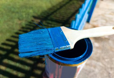 Flat brush beaver blue impregnated resting over can. Painting a wooden fence with acrylic paint clipart