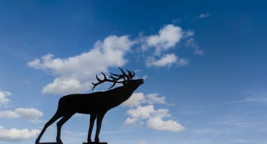 Metal plate with the silhouette of a deer indicating a big game hunting estate. Cloudy blue sky as background clipart