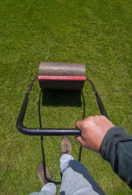 Lawn roller in action. Manual tools for lawn maintenance activities clipart