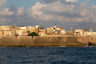 Denizden antik Akko şehrine bir kale duvarı, bir deniz feneri, bir kilise ve harap olmuş konut binalarıyla bakın.