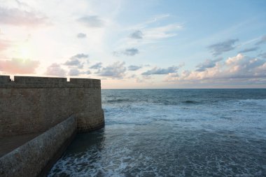 Sonbahar bulutlarıyla mavi gökyüzü ve deniz tarafından turlanan ortaçağ kalesi arasındaki ufuk.