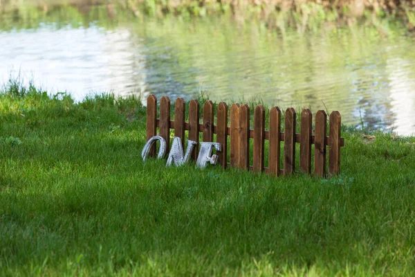 木製のスラットと川の岸の緑の芝生の単語1で作られたフェンスの断片 — ストック写真