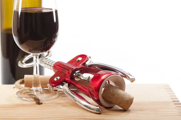 Opener with cork and glass of red wine on a wooden bottle box