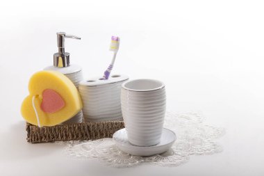 Seramik kapta bir diş fırçası, sıvı sabun için bir şişe ve sepette bir sünger, ağzınızı çalkalamak için bir bardak ve bir tabak.
