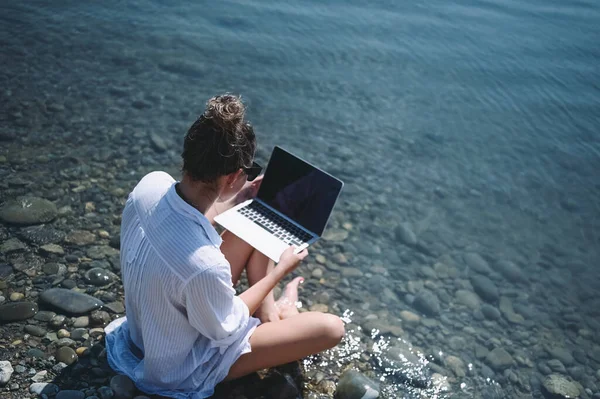 프리랜서 여행자가 셔츠를 야외에서 노트북으로 풍경을 감상하며 온라인으로 일하고 해변에서 로열티 프리 스톡 이미지