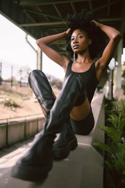 ファッション屋外ストリートスタイルの肖像画美しい若いアフリカ系アメリカ人の女性は 都市景観夏の日に総黒の高い革のブーツを着て外にポーズ — ストック写真