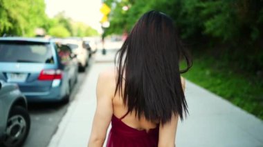 Güneşli yaz gününün dışında yürüyen güzel, genç, Asyalı mutlu bir kadının sokak tarzı portresi. Çekici bir kadın park halindeki arabaların önünde poz vermekten hoşlanır. Büyük şehir hayatı konsepti