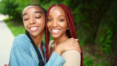 Sokak tarzı güzel Afro-Amerikan kadın siyah çift portresi. Saç örgüsü, mükemmel beyaz dişler, kız kardeş arkadaşlar güneşli bir yaz gününde dışarıda yürüyorlar. Yeşil park ve şehir