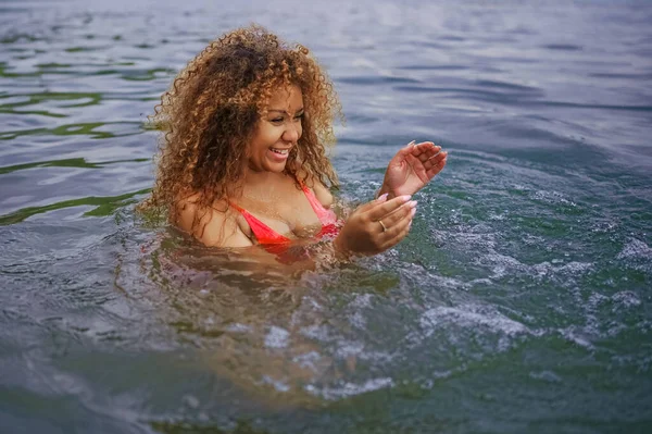 Çekici mutluluk artı boyut Afro-Amerikan siyahi kadın açık havada deniz gölü suyunda su sıçratarak yüzmeyi seviyor.