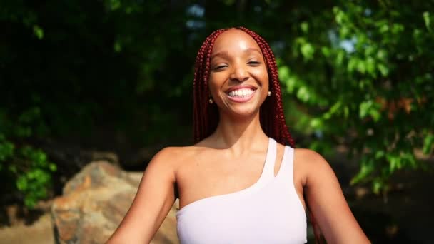 屋外の肖像画自然美しい若いアフリカ系アメリカ人の女性赤い毛のスタイル 完璧な白い歯の笑顔 緑の葉の背景と晴れた夏の日に手で閉じるカメラを笑って — ストック動画