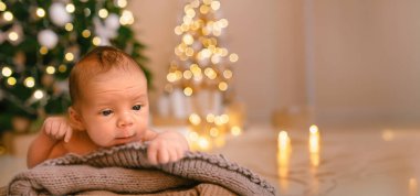 Yeni yıl tatili sahnesi. Yeni doğan komik bebek, Noel ağacı oyuncakları ve ışık çelengi ile örülü battaniyede yatıyor. Bebek eşyaları konsepti, kreş